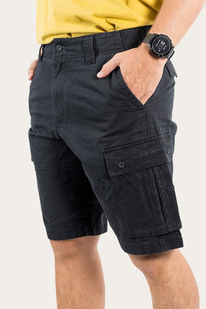 A person wearing a yellow Ringers Western shirt and black Ringers Western Gawler Cargo Short with one hand in the shorts pocket. The person also has a smartwatch on their wrist. The background is plain and light-colored.