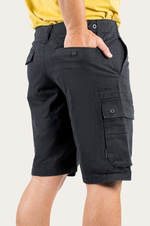 A person is wearing a pair of Ringers Western Gawler Cargo Shorts, made from 100% cotton, with hands partially in the side pockets. The shorts feature buttoned flap pockets on the sides and back. The person is also wearing a yellow shirt, which is partially visible.