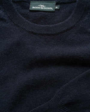 A close-up of a dark blue wool sweater with a crew neck, showcasing the "Rodd & Gunn" tag at the neckline. The knit texture is prominent, and it looks soft, plush, and lightweight; it's the Rodd & Gunn Queenstown Sweater.