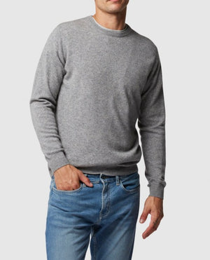 A man wears the Rodd & Gunn Queenstown Sweater in gray wool paired with blue jeans, standing with one hand in his pocket against a plain white background.