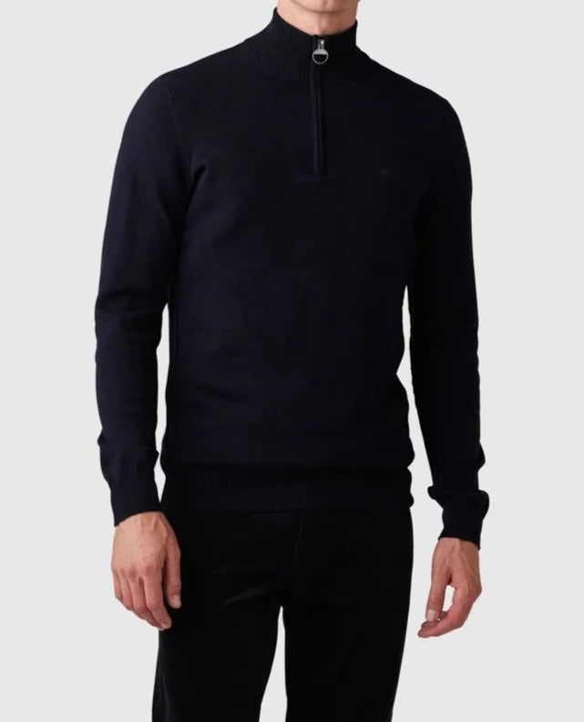 A man is wearing a Rodd & Gunn Bishopsdale Knit, a dark, long-sleeve Australian Merino quarter zip jumper. The zipper is partially open, revealing a high collar. He pairs this stylish knit with dark pants against a plain white background, showcasing only his upper body.