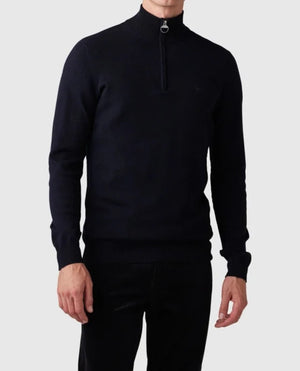 A man is wearing a Rodd & Gunn Bishopsdale Knit, a dark, long-sleeve Australian Merino quarter zip jumper. The zipper is partially open, revealing a high collar. He pairs this stylish knit with dark pants against a plain white background, showcasing only his upper body.