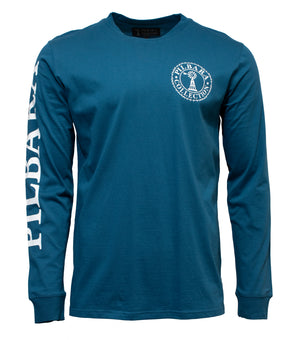 The Pilbara Long Sleeve T-Shirt is a casual blue top with a round neck, made from 100% cotton. It has "Pulaski" in white on the left sleeve and a circular logo with "Pulaski Collection" around a tree on the upper left chest. Ideal for relaxed days.
