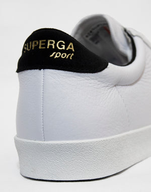Close-up of a Superga Clubs Comfleasueu Sneaker, featuring a black heel tab with gold "SUPERGA sport" lettering. The shoe is on a white background, highlighting its textured leather surface and sleek design.