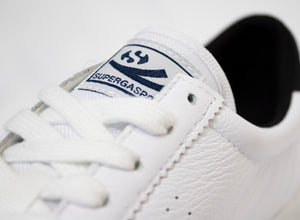 Close-up of a sleek white leather sneaker with pristine laces, showcasing a stitched label on the tongue featuring Superga's circular logo and "SUPERGASPO." The fine texture and intricate stitching highlight the Superga Clubs Comfleasueu Sneaker.
