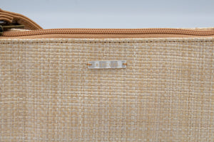 Close-up of the beachy beige woven texture of the Rip Curl Sunset Palms Shoulder Bag, featuring a central silver label saying "Rip Curl." A light brown zipper adorns the top edge, suggesting elegance and function.