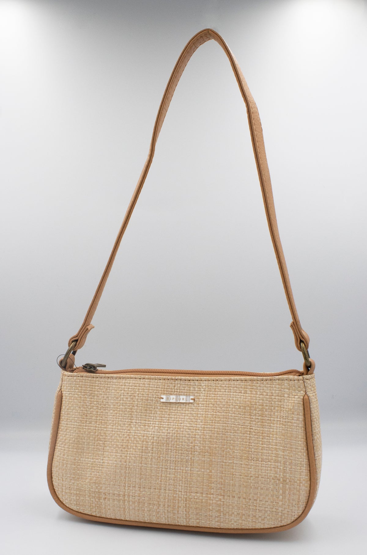 The Rip Curl Sunset Palms Shoulder Bag features a stylish beige woven design with a long tan leather strap, compact rectangular shape, and small metal logo on the front. It's displayed against a plain white background, making it ideal for casual outings with its beachy vibe.