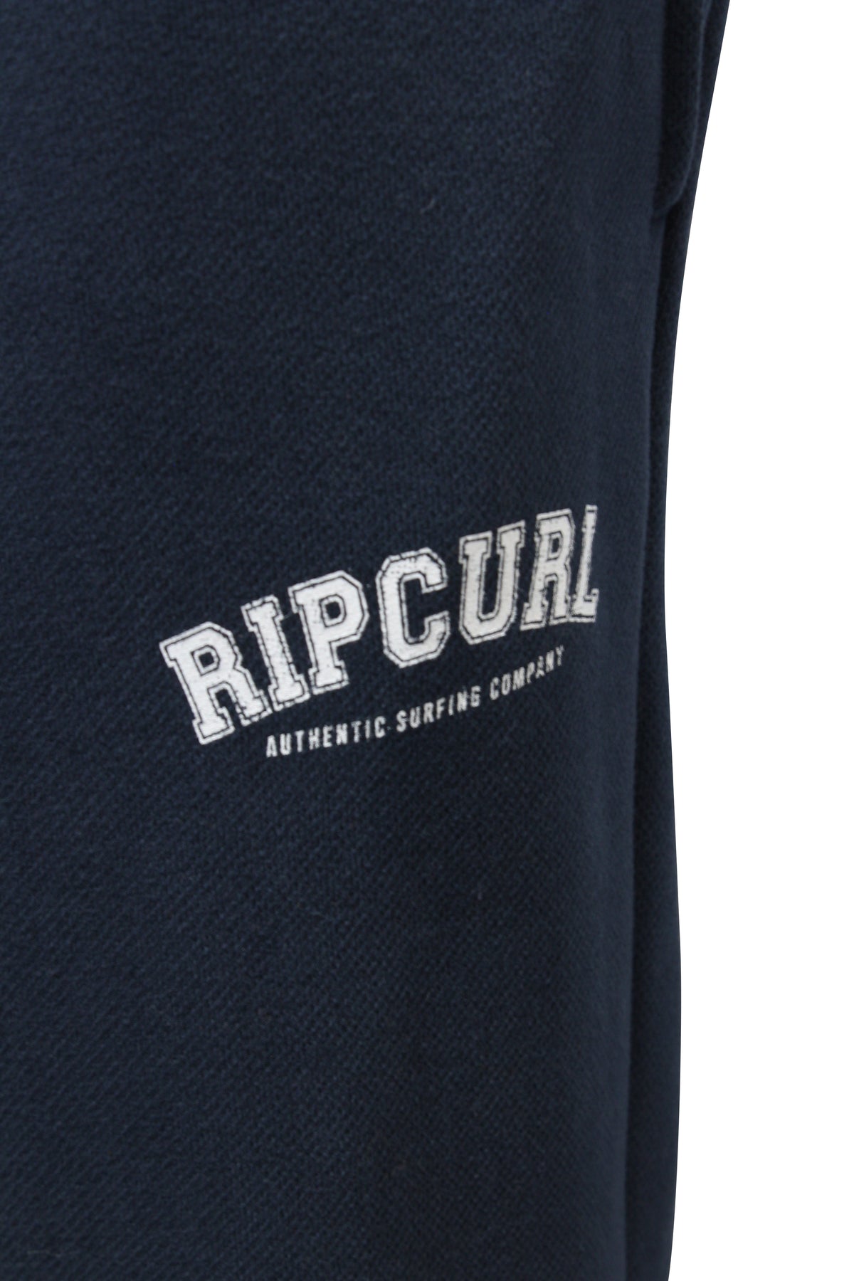 Close-up of Rip Curl Varsity Pants, featuring dark blue fabric with "Rip Curl Authentic Surfing Company" in white text. Ensure the perfect fit by selecting the correct size and consult customer service for any sizing inquiries.