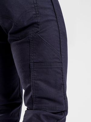 Close-up of the side of a person's leg wearing the Levis Workwear 511 Utility Pant in dark blue. The pants feature multiple seams and a large pocket on the side, highlighting the texture and structure of the fabric. The comfortable fit resembles slim stretch jeans, set against a plain, light grey background.