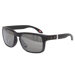 The Oakley Holbrook sunglasses feature a black frame with polarised lenses, a metallic logo near the hinge, and Prizm technology for enhanced optics. They sport a white accent on the temple and are angled against a white background, exuding sleek sophistication.