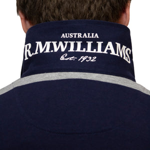 Close-up of the back of a person's neck, wearing a navy blue RM Williams Tweedale Rugby jumper with grey stripes. The text "R.M.WILLIAMS" in large white letters is visible, along with "Australia" above and "Est. 1932" below. Made from heavy weight jersey knit and 100% cotton, only the back of the person's head and neck are shown.