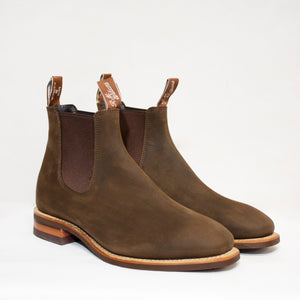 The RM Williams Comfort Craftsman Boot features brown leather, elastic side panels, brown pull tabs, and wooden soles in the iconic Chelsea style, shown against a white background.