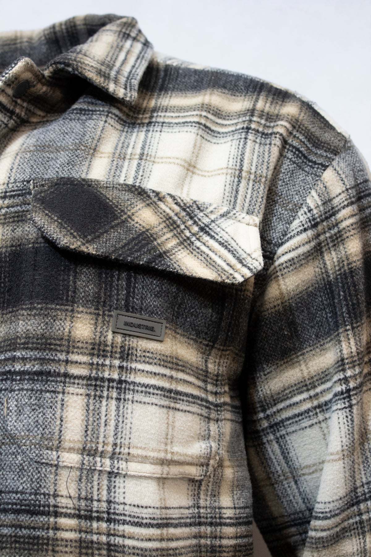 Close-up of Industrie The Morelock Overshirt in black, gray, and beige plaid flannel with a buttoned chest pocket. Made from soft polyester, it features a cozy feel and mixed stripe patterns that highlight Industrieβs attention to detail.