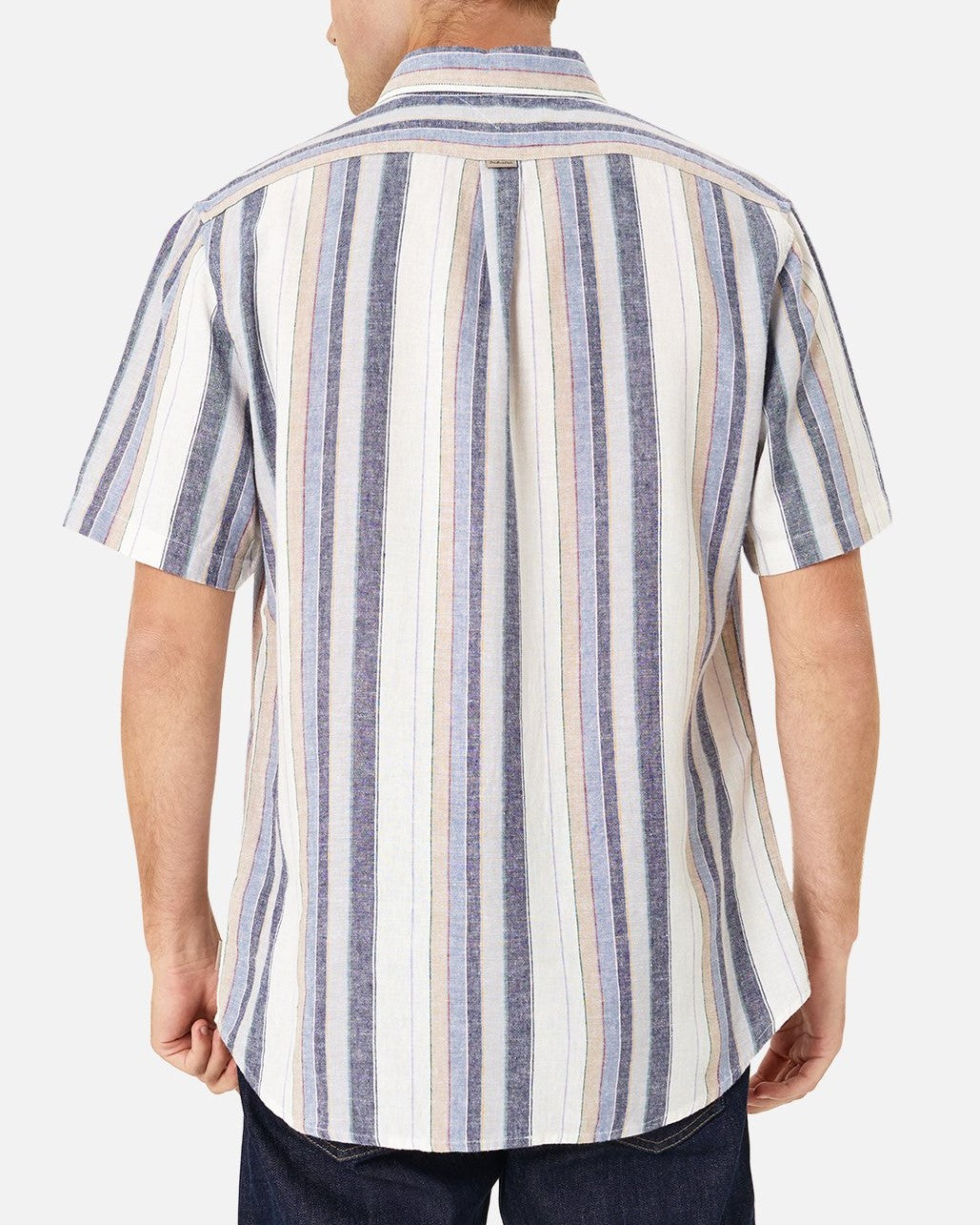 A person is seen from behind, wearing the Industrie The Tobago Shirt, a lightweight, short-sleeved, button-up shirt with vertical stripes in blue, white, and beige tones. The shirt is untucked, and the person is also wearing dark blue jeans. The background is white.