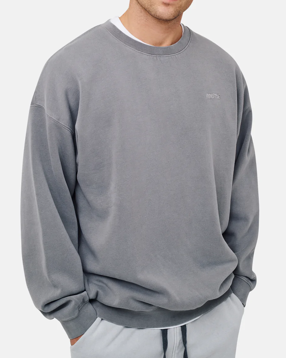 A person in an oversized grey "Industrie The Del Sur Sweat" with chest stitching, paired with light gray sweatpants, stands against a plain background with hands in pockets.