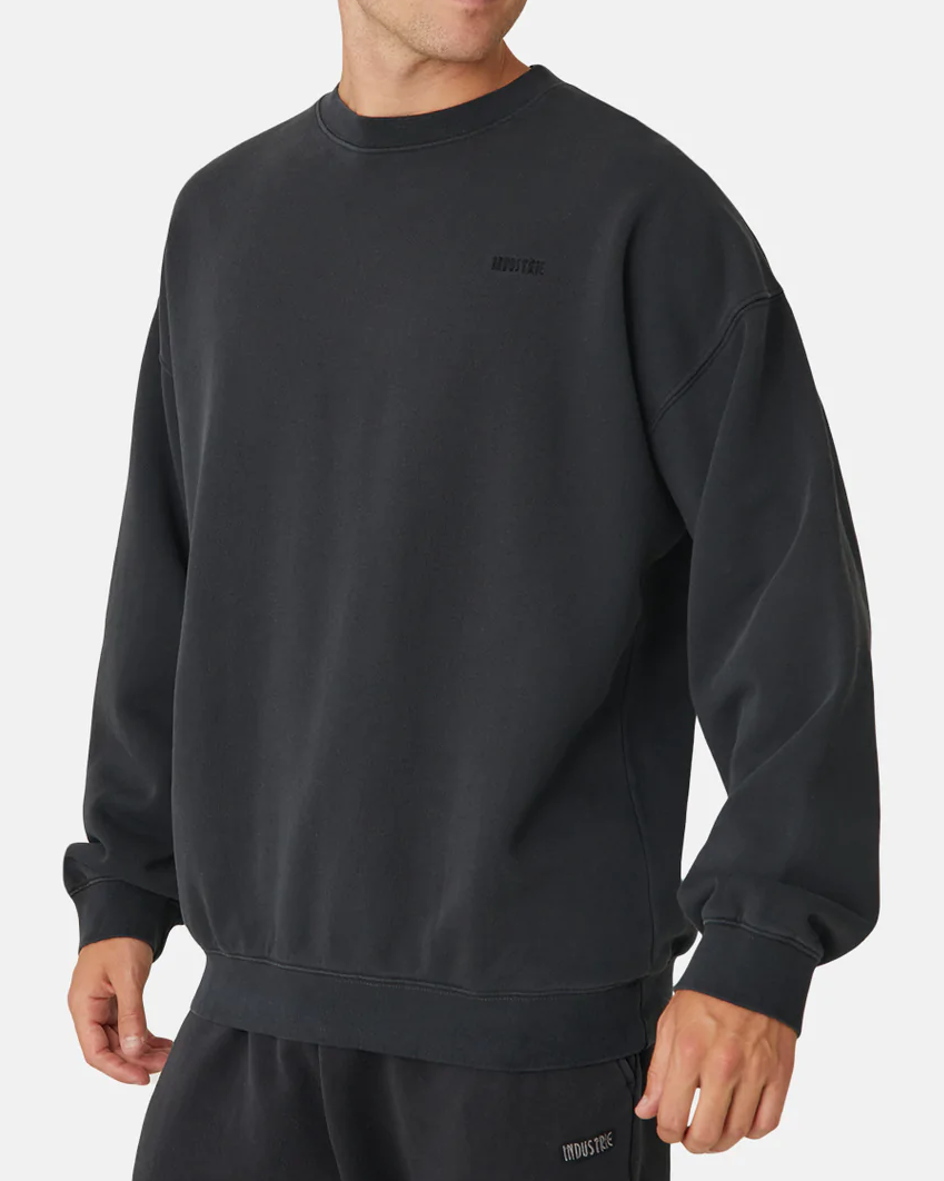 A person in an oversized dark gray Industrie The Del Sur Sweat with matching sweatpants stands against a light background. The relaxed fit and small chest logo enhance its acid wash vibe, adding a casual style touch.