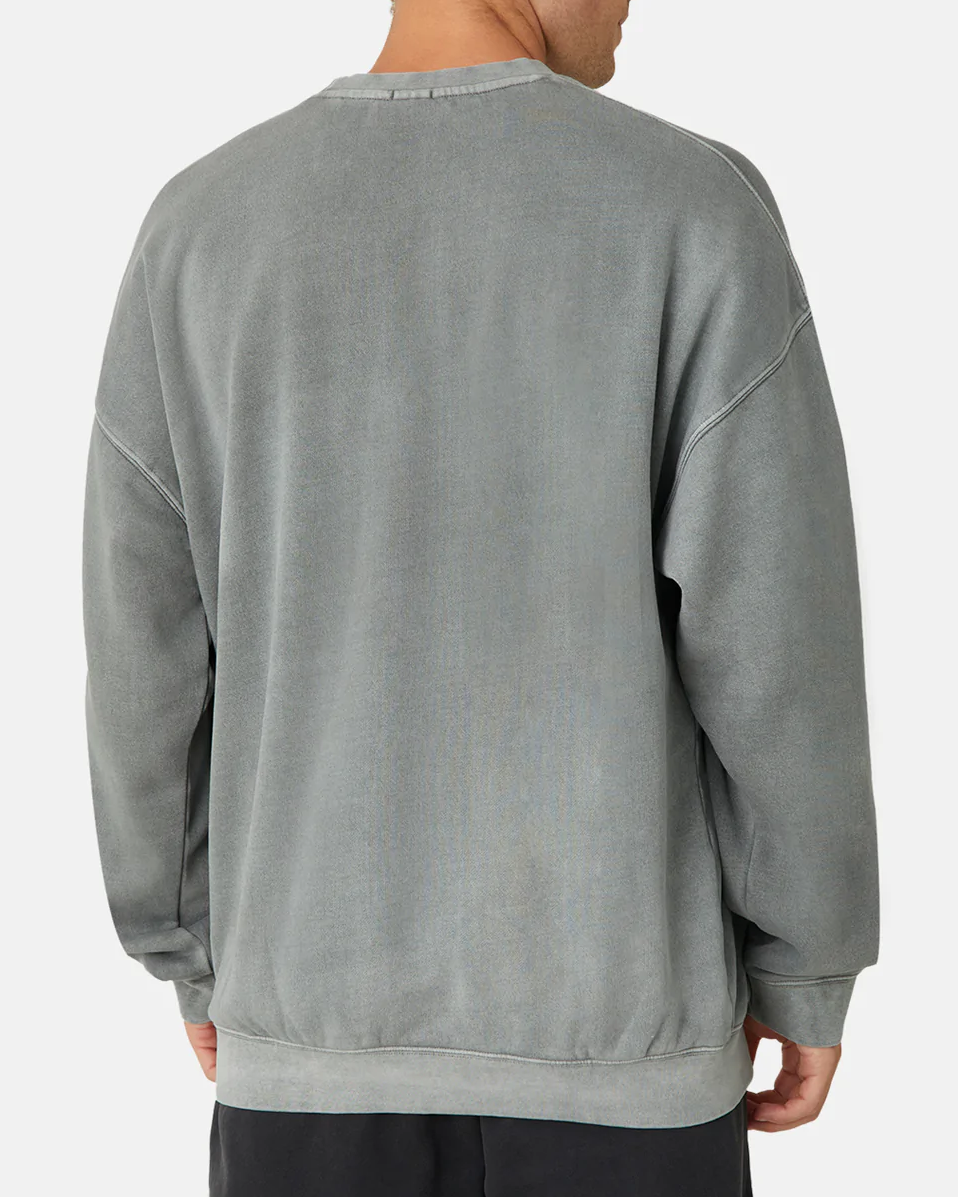 A person wears the Industrie The Del Sur Sweat, a comfortable jumper with an oversized fit. With a faded gray color, it has a crew neck, dropped shoulder seams, and subtly displays the logo. They pair it effortlessly with dark pants.