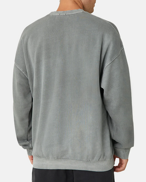 A person wears the Industrie The Del Sur Sweat, a comfortable jumper with an oversized fit. With a faded gray color, it has a crew neck, dropped shoulder seams, and subtly displays the logo. They pair it effortlessly with dark pants.