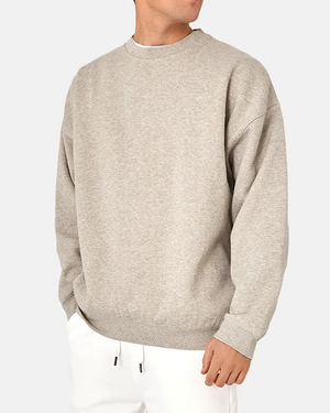 Someone is wearing the Industrie The Del Sur Sweat in light gray with long sleeves and subtle chest embroidery, paired with white pants. The oversized fit and plain light gray background enhance the outfit's relaxed vibe.