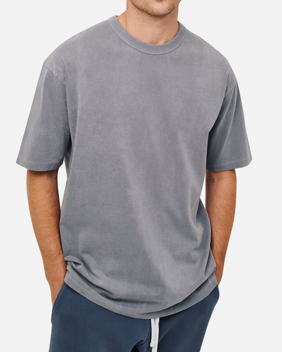 Someone wearing an oversized Industrie The Del Sur Tee in gray, paired with dark gray pants, stands casually with their hands in pockets against a white background.