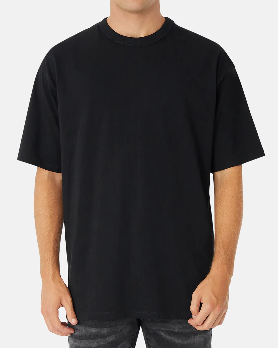 A person in an oversized black Industrie The Del Sur Tee, made from 100% cotton with short sleeves and a round neckline, stands against a white background. Their hands rest by their sides, highlighting the tee's effortless style.