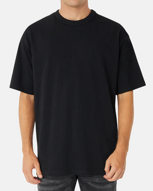 A person in an oversized black Industrie The Del Sur Tee, made from 100% cotton with short sleeves and a round neckline, stands against a white background. Their hands rest by their sides, highlighting the tee's effortless style.