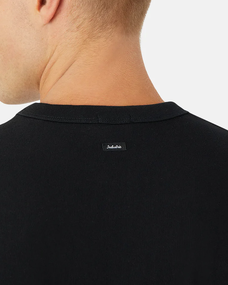 A person wears the Industrie The Del Sur Tee in an oversized black fit, shown from the back with focus on the neck area. A small black label is visible near the neckline on this comfortable shirt, against a plain white background.