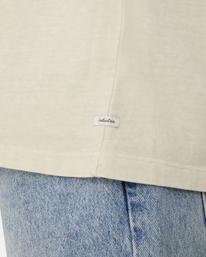 Close-up of the cream-colored Industrie The Del Sur Tee, crafted from 100% cotton with an oversized fit for comfort. A small "industrie" label is visible. This tee pairs perfectly with light blue denim jeans for a relaxed yet stylish look.