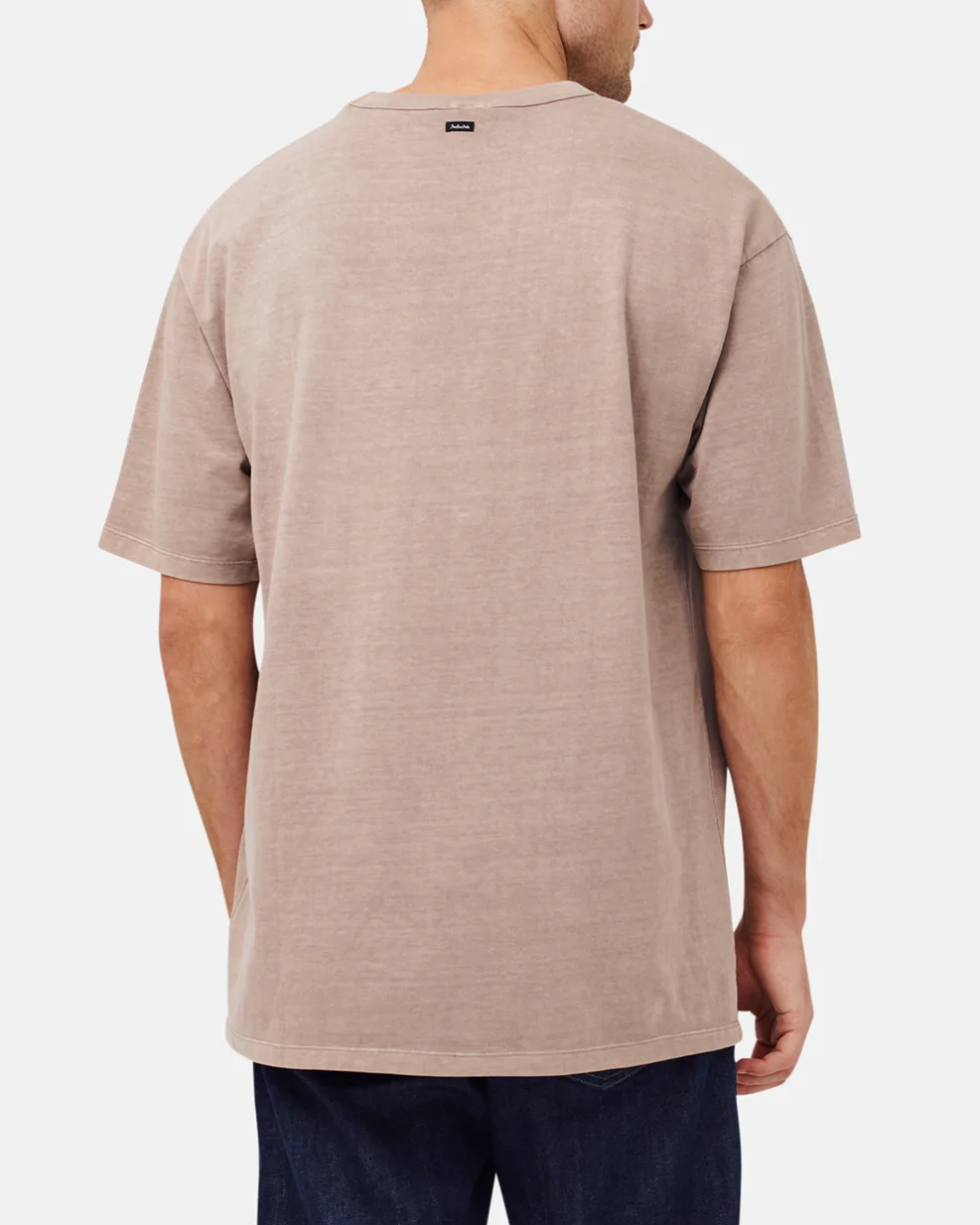 Someone in an oversized Industrie The Del Sur Tee, in beige with a simple design and small neckline tag, wears dark jeans. The acid wash finish gives the tee a unique texture, standing out against the plain white background.