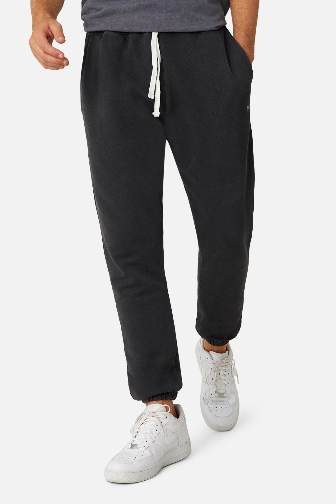A person wearing Industrie The Del Sur Track Pant with an elastic drawstring waist and white sneakers is walking. The joggers feature an embroidered Industrie logo, complementing their dark top. Only the lower half is visible, highlighting a blend of comfort and style.