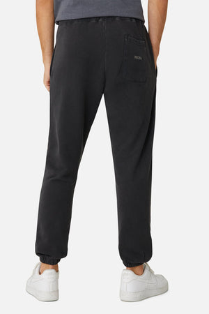 A person is seen from behind wearing Industrie The Del Sur Track Pant in black, featuring an embroidered logo on the back pocket, paired with white sneakers. The joggers offer an elastic drawstring waist for comfort against a plain white backdrop.