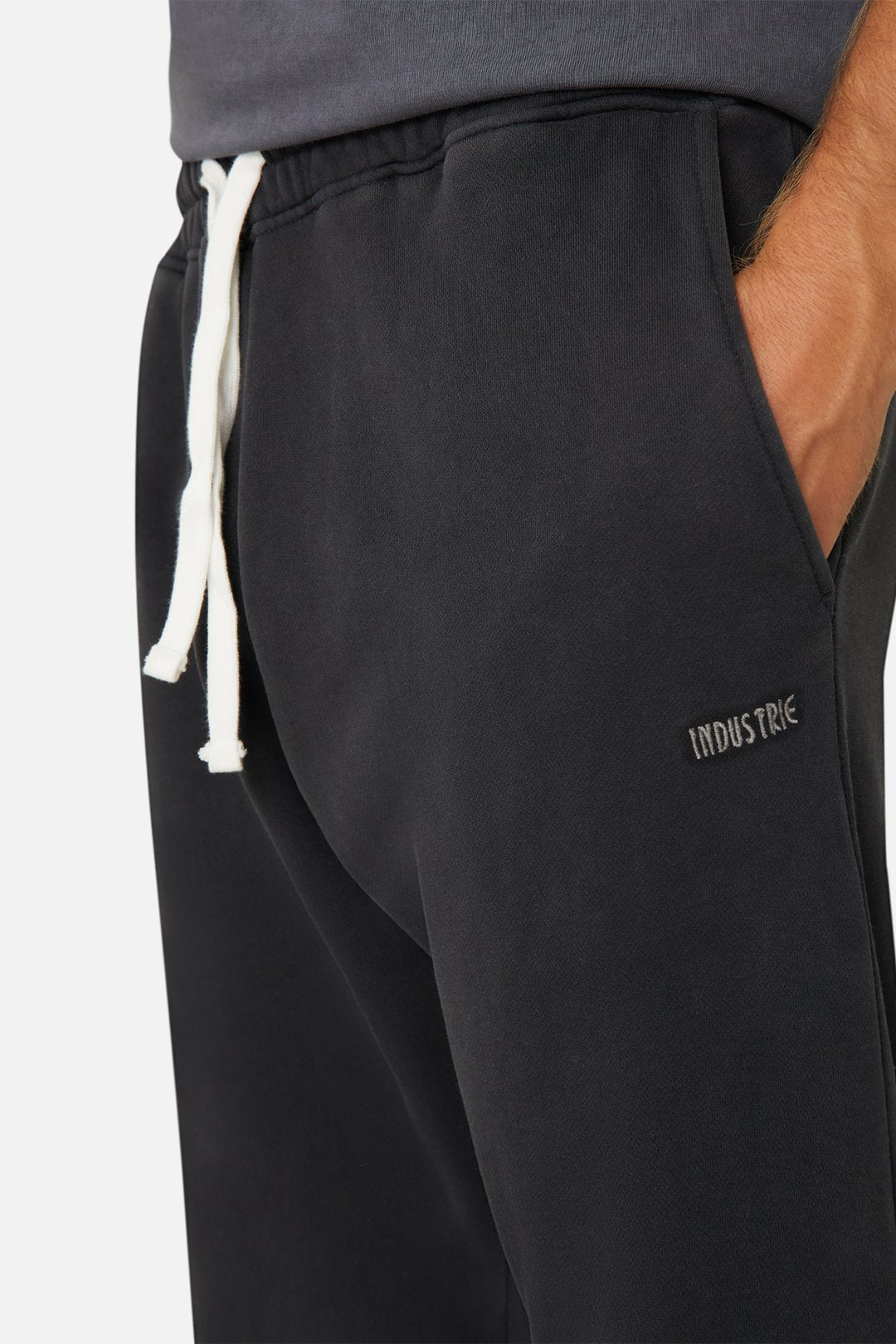 Close-up of a person wearing Industrie The Del Sur Track Pant in black, featuring an elastic drawstring waist and embroidered logo on the side. The person has their hand in the pocket, against a plain background.