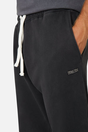 Close-up of a person wearing Industrie The Del Sur Track Pant in black, featuring an elastic drawstring waist and embroidered logo on the side. The person has their hand in the pocket, against a plain background.