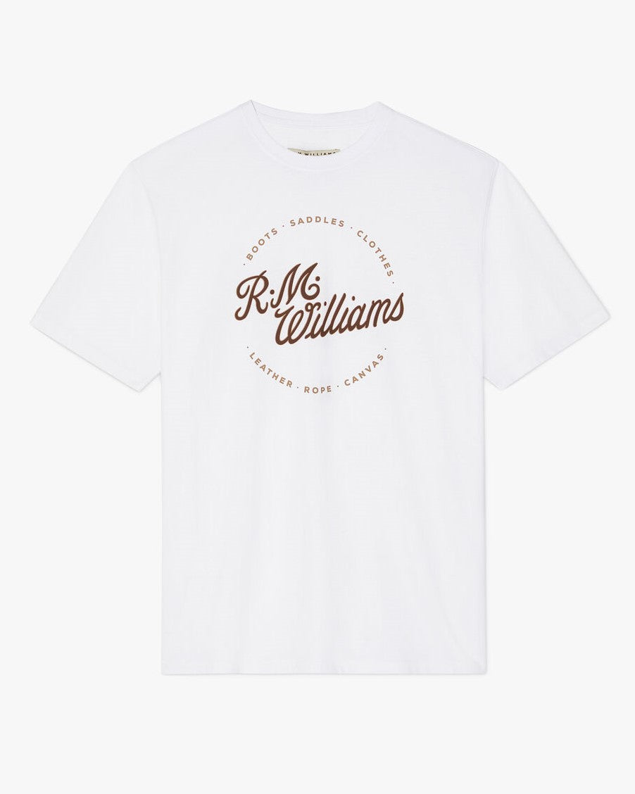 The RM Williams Script Stamp T-Shirt is a white, 100% cotton shirt featuring the brand's script logo in brown on the front, surrounded by words like "Boots" and "Saddles," blending style with comfort.