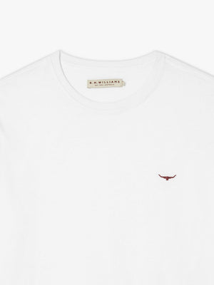The RM Williams Parson T-Shirt is a white cotton crew-neck featuring a small red bull's head logo embroidered on the left chest and a beige label with text stitched inside the collar. Its fabric looks soft and plain.