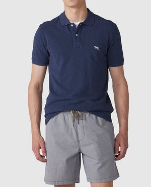 A person is wearing the Rodd & Gunn The Gunn Polo, a navy blue and comfortable shirt made from Australian Cotton, featuring a small embroidered horse logo on the chest, paired with gray drawstring shorts. The background is plain white.