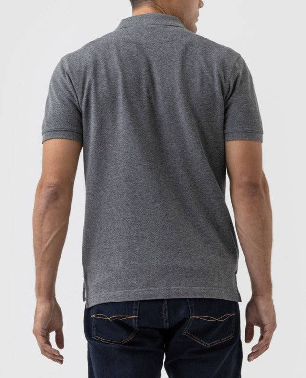 A man wearing a modern fit, short-sleeved gray Rodd & Gunn The Gunn Polo and dark blue jeans stands with his back to the camera against a plain, light background.