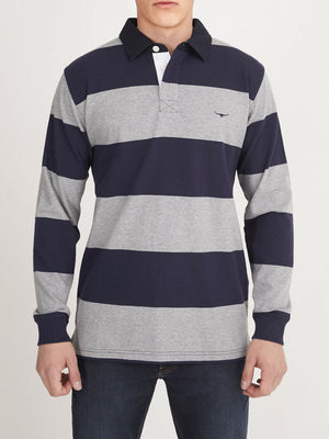 A person is wearing the RM Williams Tweedale Rugby long-sleeved shirt, crafted from heavyweight jersey knit and featuring wide horizontal navy blue and gray stripes. This 100% cotton shirt boasts a white collar and a small logo on the left chest area, paired with dark blue jeans against a plain white background.