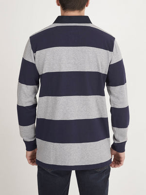 A person is standing with their back to the camera, wearing a RM Williams Tweedale Rugby shirt made of 100% cotton, featuring wide horizontal stripes in alternating navy blue and light gray colors. They are also wearing dark blue jeans. The background is plain white.