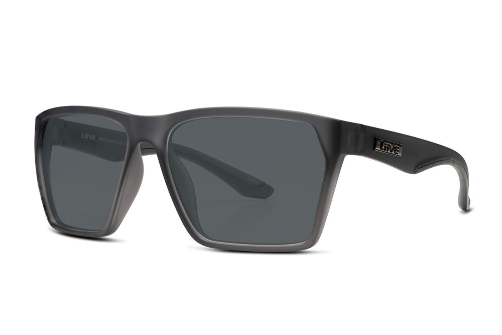 The Liive Rincon Polar Sunglasses offer excellent UV protection with stylish, thick, rectangular frames in translucent dark grey. Crafted from lightweight polycarbonate, they feature dark polarized lenses and a small metallic logo on the temple.