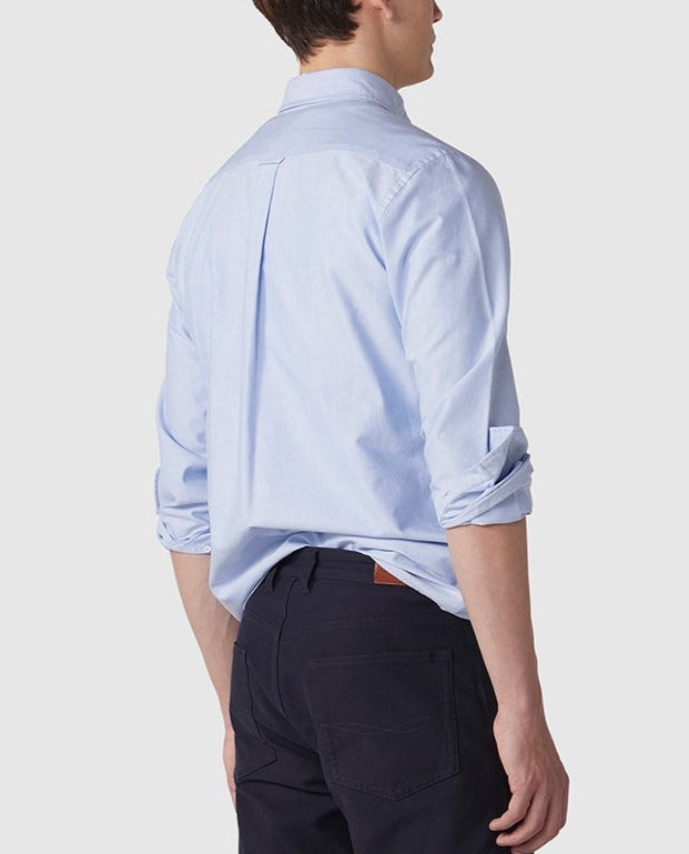 Seen from behind, a person with short hair wears the Rodd & Gunn Gunn Oxford Sports Fit Shirt in light blue, sleeves rolled up, paired with dark pants against a plain white background.