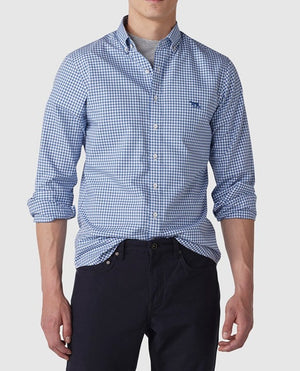 A person wearing the Rodd & Gunn Gunn Check Oxford Sports Fit Shirt, made of 100% cotton in a blue and white checkered pattern, with rolled-up sleeves and dark pants stands against a plain background. The stylish shirt features a small embroidered logo on the chest. The person's head is not visible in the image.