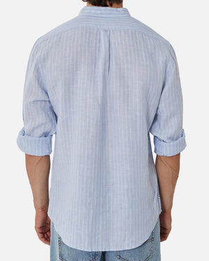 Wearing the Industrie The Mattera Long Sleeve Shirt in stylish light blue linen with vertical stripes, sleeves rolled to the elbows for a relaxed feel, paired with light blue jeans against a plain white backdrop, the look exudes comfort.