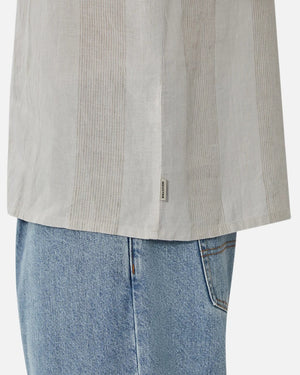 Close-up of a person wearing the Industrie The Kanaki Short Sleeve Shirt with light vertical stripes, displaying a tag on the side, paired with light blue jeans. The focus is on the lower half of the shirt and top of jeans.