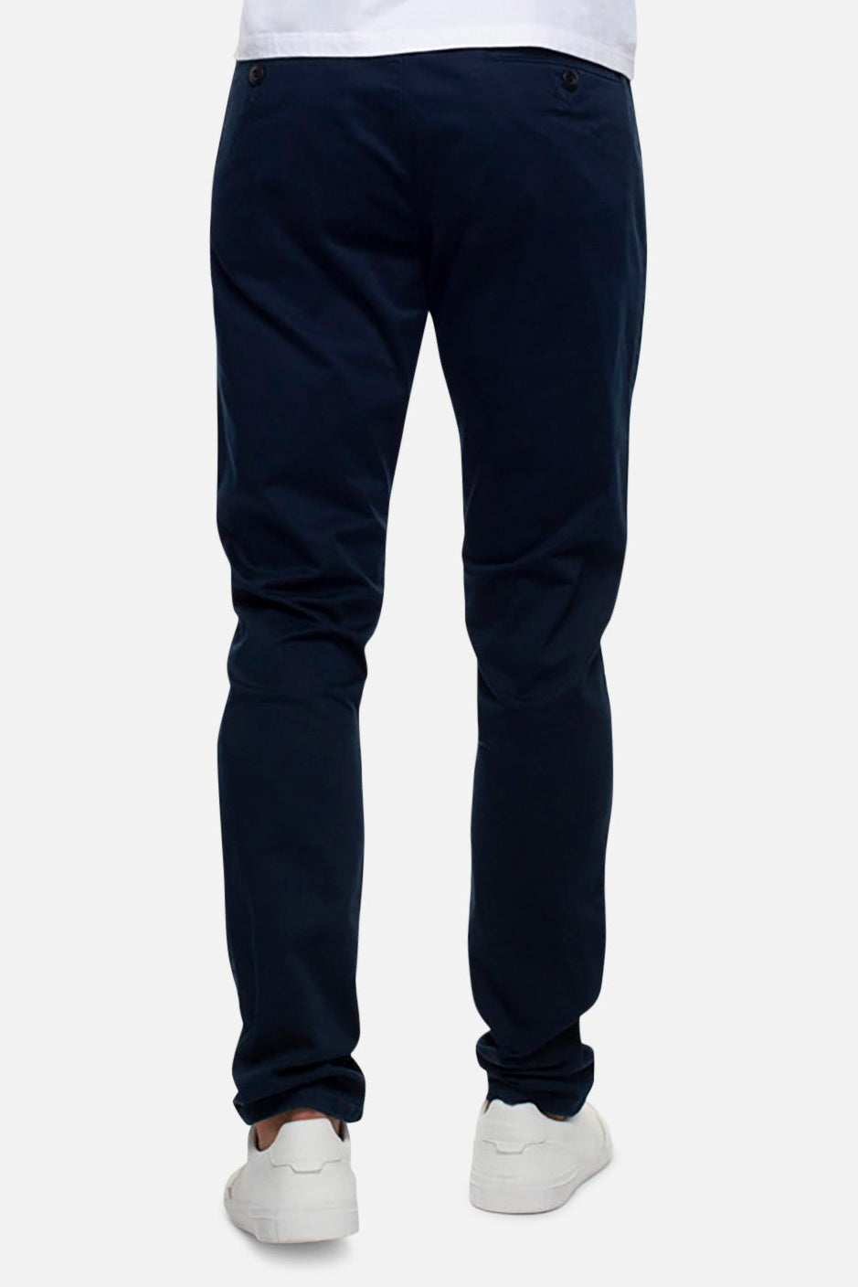 Rear view of a person wearing the Industrie The Cuba Chino Pant in dark blue and white sneakers, standing against a plain light grey background. Only their legs and lower torso are visible.