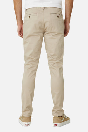 A person is seen from the back wearing Industrie The Cuba Chino Pant, a white shirt, and casual beige sneakers with white soles against a plain white background.