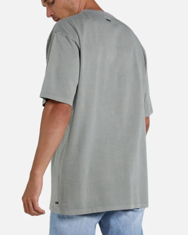 A person is wearing an oversized gray "Industrie The Del Sur Tee" and light blue acid wash jeans, standing against a plain background. They are turned slightly away, highlighting the back of the comfortable tee and their side profile.