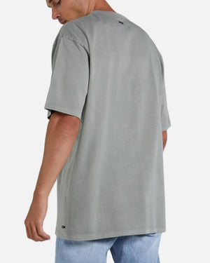 A person is wearing an oversized gray "Industrie The Del Sur Tee" and light blue acid wash jeans, standing against a plain background. They are turned slightly away, highlighting the back of the comfortable tee and their side profile.