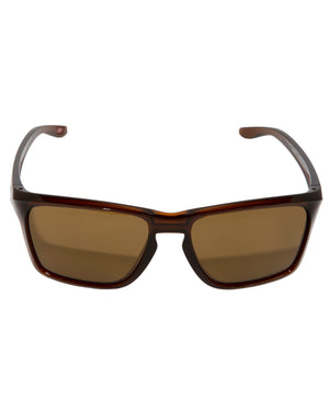 A pair of Oakley Sylas sunglasses featuring a polished Rootbeer frame, dark brown rectangular lenses with Prizm technology for enhanced clarity, and slightly curved temples is displayed against a white background.