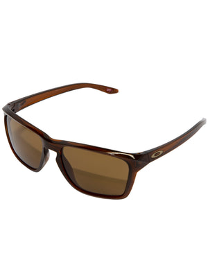 A pair of Oakley Sylas sunglasses featuring a polished Rootbeer frame and rectangular, brown-tinted Prizm lenses that are slightly curved to fit the contours of the face. The sleek, modern design is highlighted by small, oval-shaped logos on the temples.